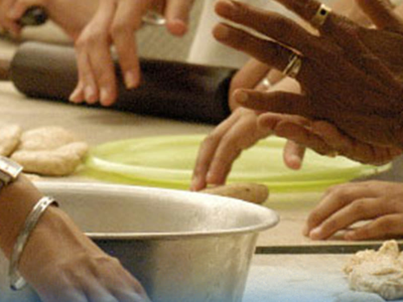 Many hands rolling and shaping dough together at a community kitchen table